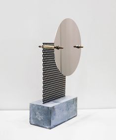 a sculpture made out of metal on top of a cement block in front of a white wall