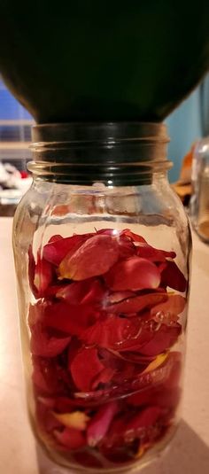 a glass jar filled with red petals on top of a table next to a green bowl