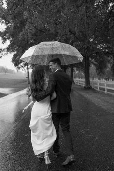 a man and woman walking in the rain with an umbrella over their heads, holding each other's hands