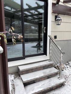 snow is falling on the steps leading up to a door with glass and metal railing