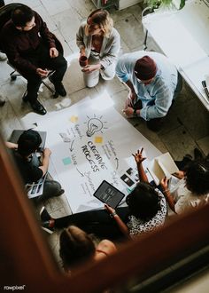 several people sitting around a table with papers and laptops on it, looking down at the floor