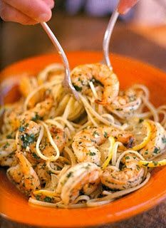 someone is eating pasta with shrimp and lemons in a orange bowl on the table