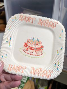 a person holding up a paper plate with a birthday cake on it