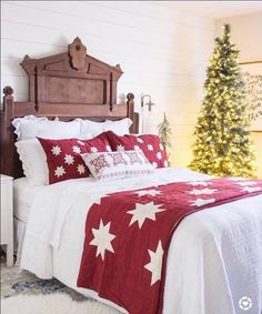 a bed with red and white comforter next to a christmas tree in a bedroom