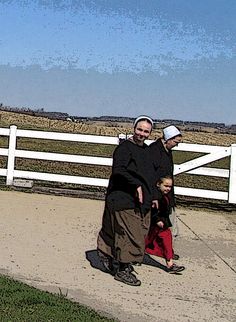 two people walking down a sidewalk near a white fence with a blue sky in the background