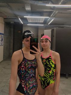 two women in swimsuits standing next to each other holding up a cell phone