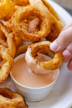 onion rings on a plate with dipping sauce in the middle and hand reaching for one