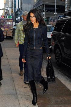 a woman is walking down the street with her hand in her pocket and wearing black boots