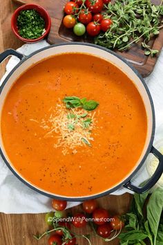 a bowl of tomato soup with parmesan cheese on top and fresh tomatoes in the background