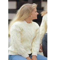 a woman sitting on the ground wearing a white sweater