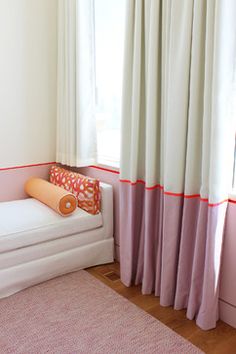 a white couch sitting next to a window in a room with pink walls and curtains