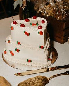 a white cake with cherries on it sitting on a table next to silverware