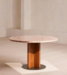 a round table with a wooden base in an empty room on the floor and white walls