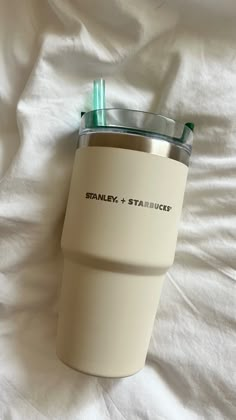 the tumbler cup is sitting on top of the white bed sheet and has a straw in it