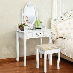 a bedroom with a white bed, vanity table and mirror on the wall next to it