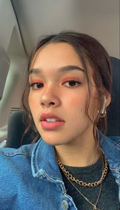 a young woman wearing a denim jacket and gold necklace, sitting in the back seat of a car