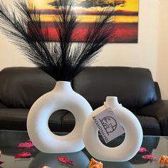 two white vases sitting on top of a glass table next to a black couch