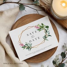 a save the date card sitting on top of a wooden plate next to a candle