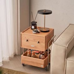 a small wooden table with two drawers on it next to a white couch and window