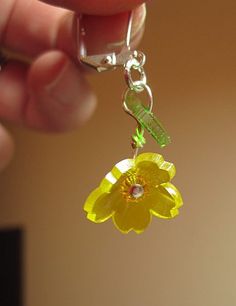 a hand holding a yellow flower shaped keychain with a green leaf on it