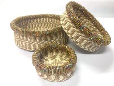 three woven baskets sitting on top of a white table next to each other with beaded handles