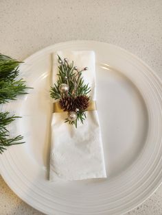 a white plate topped with a napkin covered in pine cones and greenery on top of it