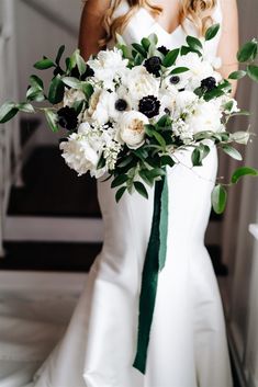 a bride holding a bouquet of white and black flowers in her hand while standing on the stairs