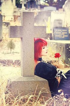 a woman with red hair is sitting in front of a grave holding a single flower