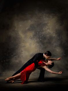 a man and woman dance together in front of a dark background, with their arms around each other