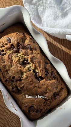 a loaf of chocolate chip banana bread in a white casserole dish on a wooden table