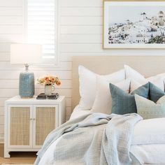 a bed with white sheets and pillows in a bedroom next to a painting on the wall