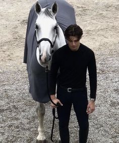 a man standing next to a horse with a blanket on it's head and holding the reins