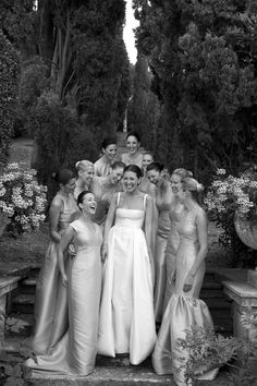 a group of women standing next to each other in front of trees and bushes with flowers