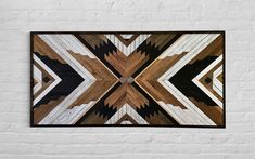 a wooden wall hanging on the side of a white brick wall with an abstract design