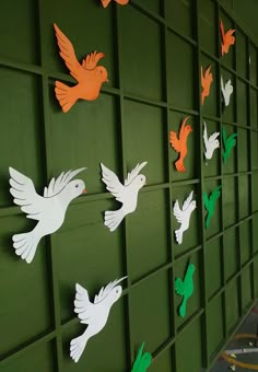 several paper birds on a green wall with orange and white ones in the air above them