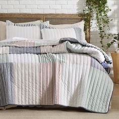 a bed with white and blue striped comforter next to a plant in a pot