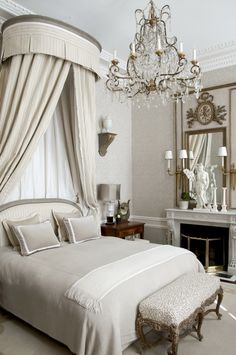 a white bed sitting in a bedroom next to a fire place under a chandelier