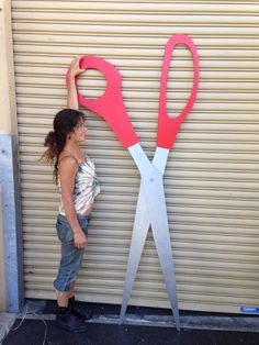 a woman standing in front of a pair of red scissors with the handles cut out