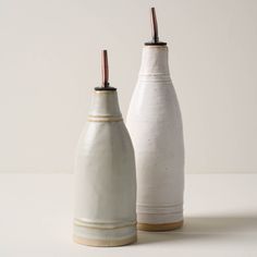 two white vases sitting next to each other on top of a table, one with a brown handle