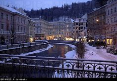 a river running through a city next to tall buildings covered in snow at night with lights on