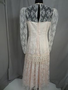 "Wonderful color and feminine styling on this vintage blush pink lace dress. It has a very pretty high neckline. The label is a mystery, only a paper tag sewn on says 11/12 and a code 5414 . Pink lining fabric has a sturdy feel and nice thickness. Lace overlay is sheer. Shape is very feminine, long sleeves with a drop waist. Waist has an extra layer of floral lace. Back zipper. Full skirt. Please convo me for any additional details or photos you would like. Marked size 11/12 but these sizes are Spring Vintage Lace Dress With Lace Work, Fitted Vintage Lace Dress For Spring, Vintage Pink Dresses With Lace Patchwork, Vintage Pink Dress With Lace Patchwork, Vintage Lace Dresses With Lace Patchwork, Vintage Lace Fitted For Party, Vintage Style Fitted Lace For Party, Vintage Fitted Lace For Parties, Spring Vintage Lace Dress With Lace Sleeves