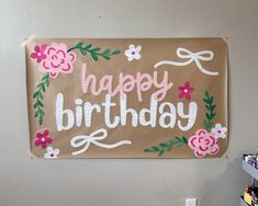 a sign that says happy birthday with flowers and leaves on the front, hanging on a wall