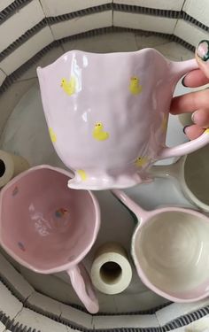 a person holding a pink coffee cup with yellow rubber ducks on it and other cups