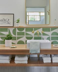 a bathroom with green and white tiles on the wall, wooden countertop and sink