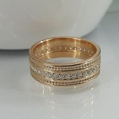 two gold wedding bands sitting on top of a white table next to a bowl filled with flowers