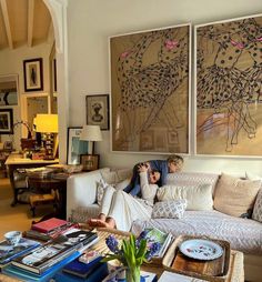 a woman sitting on top of a couch next to a child in front of paintings