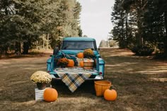 an old blue truck with pumpkins and flowers on the back parked in a field