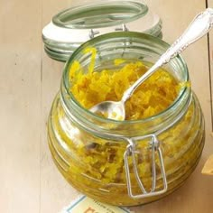 a jar filled with yellow food next to a bowl of tortilla chips and a spoon