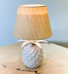 a white pineapple lamp sitting on top of a table next to a beige shade