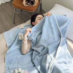 a woman laying on top of a bed under a blue blanket next to a cat